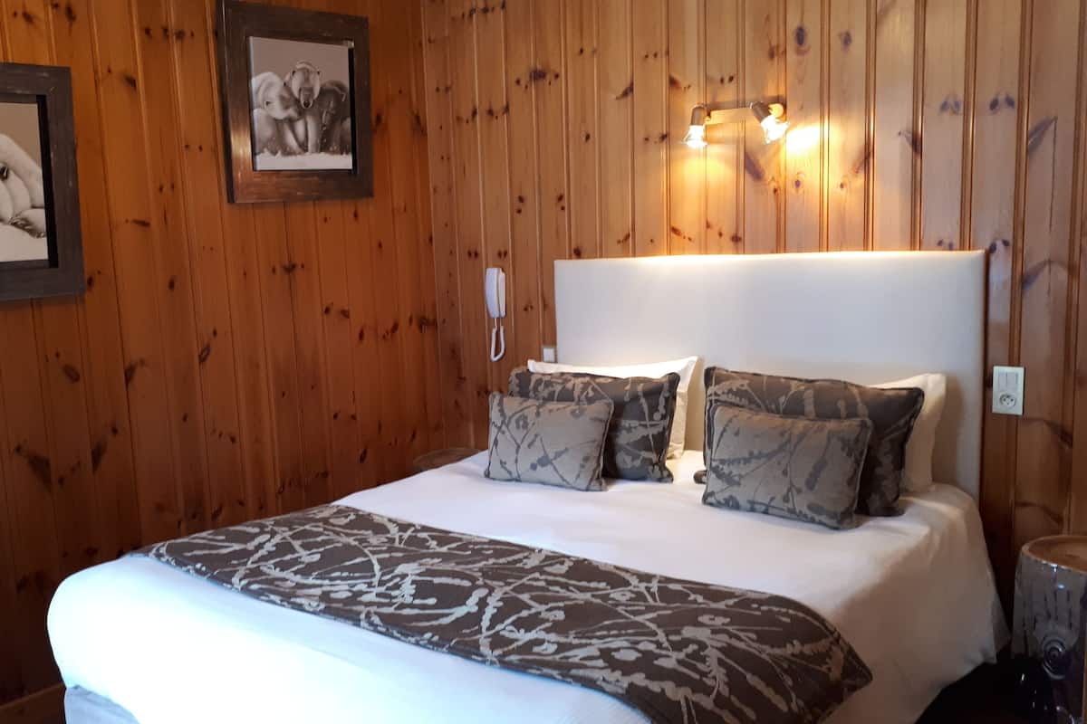 Ein Zimmer mit Holzwandverkleidung, einem Bett, zwei gerahmten Bildern, einem Nachttischtelefon und Wandleuchten.