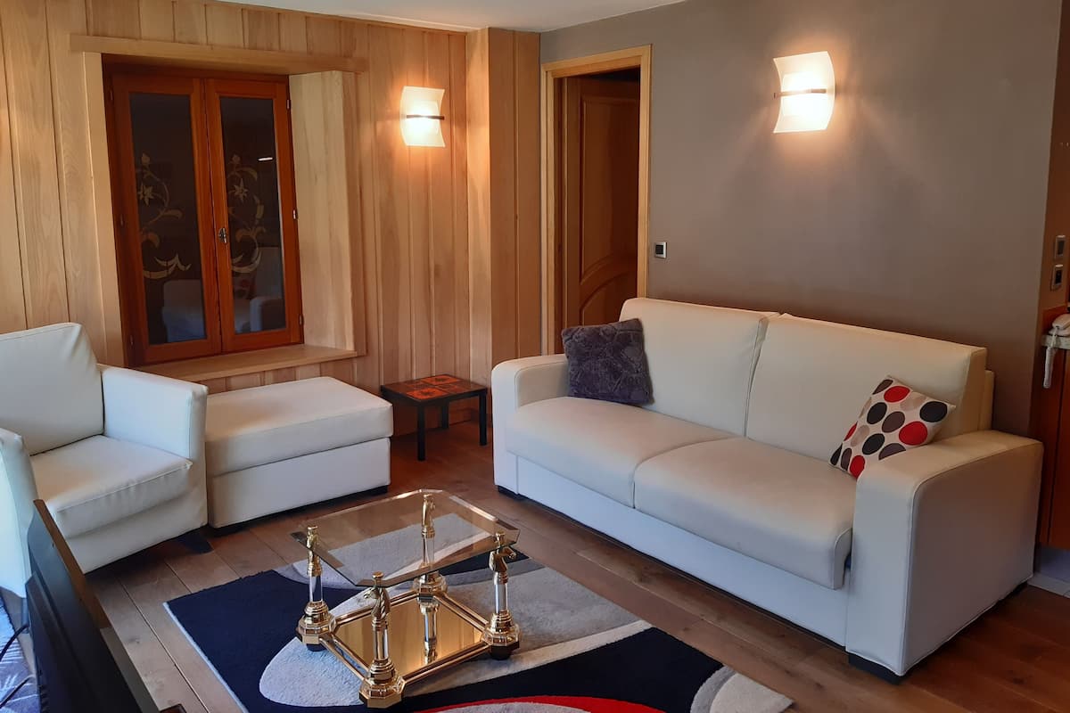 Ein modernes Wohnzimmer mit einem weißen Sofa, zwei weißen Sesseln, einem Glastisch und einer Holzvitrine.