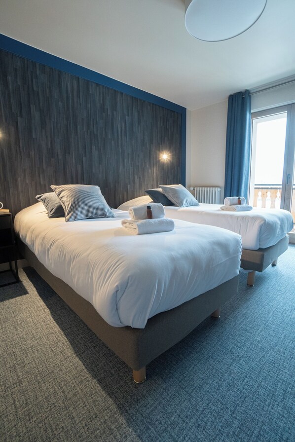 Habitación de hotel con dos camas, un muro decorativo de madera, un ventanal con cortinas y suelo alfombrado.