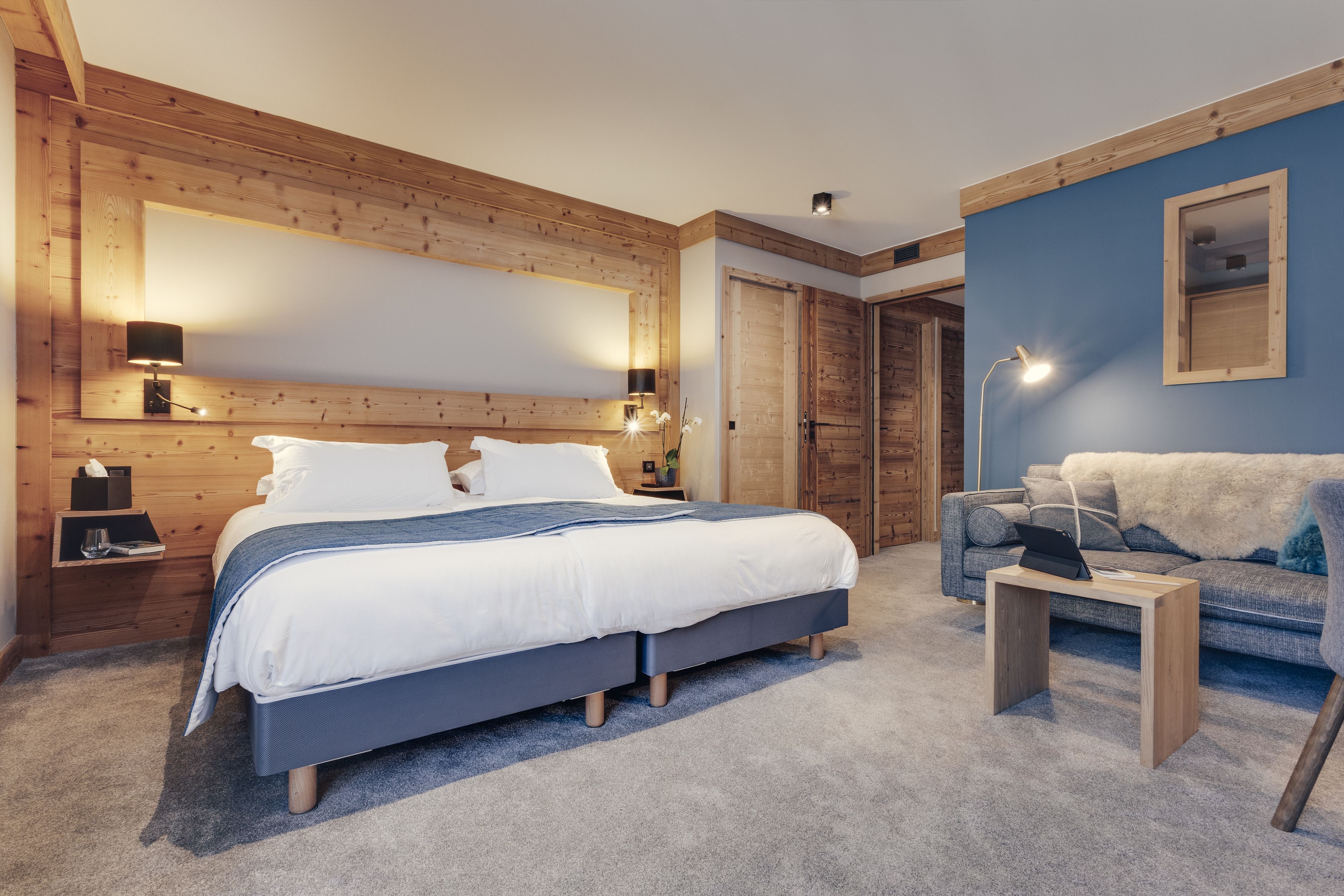 A bedroom with a bed, bedside tables, a lamp, a sofa, and a wooden wall.