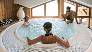 A hot tub with two people, wooden walls, and large windows.