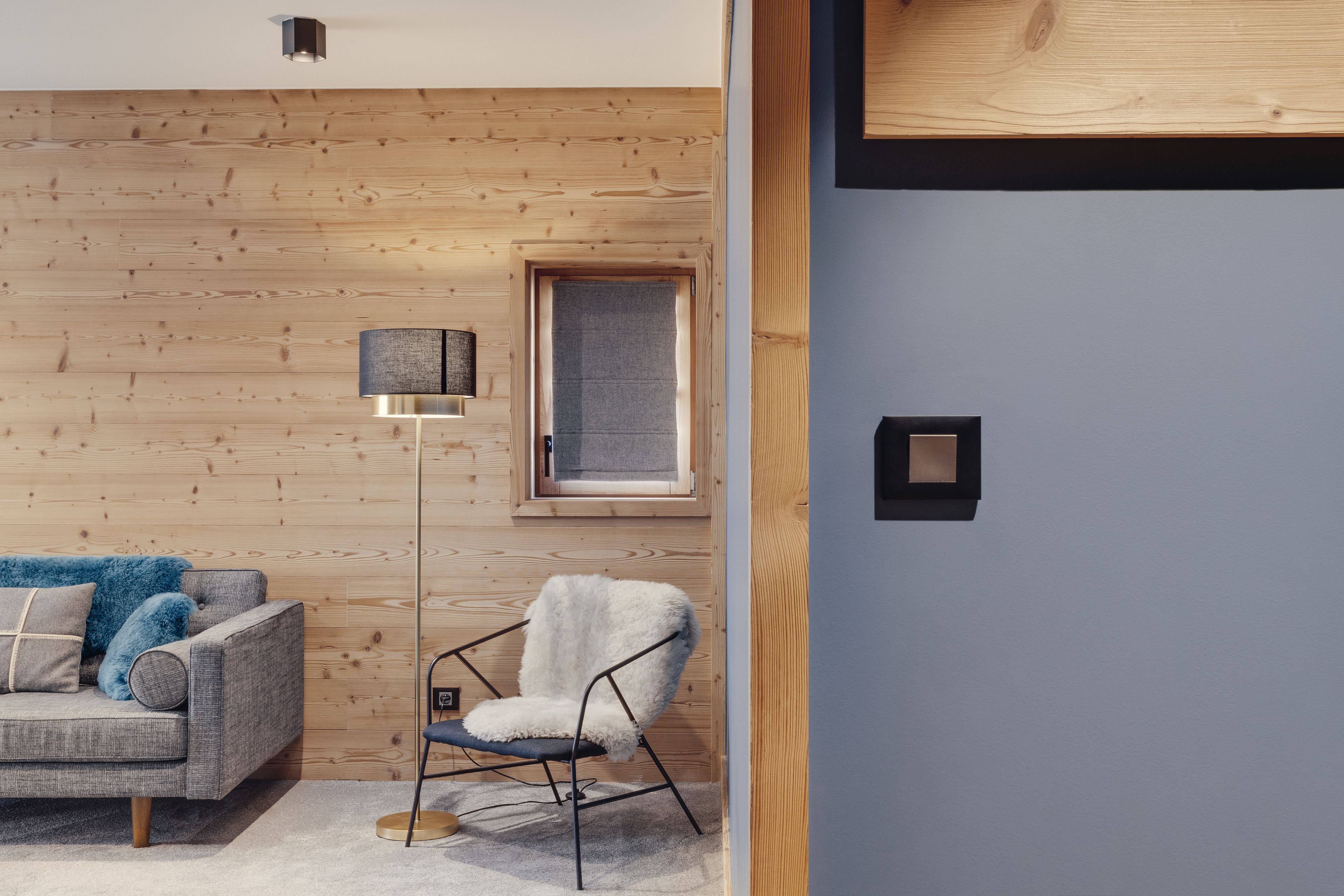 Ein modernes Wohnzimmer mit einer Holzwand, einem grauen Sofa, einem weißen Sessel und einer Stehlampe.
