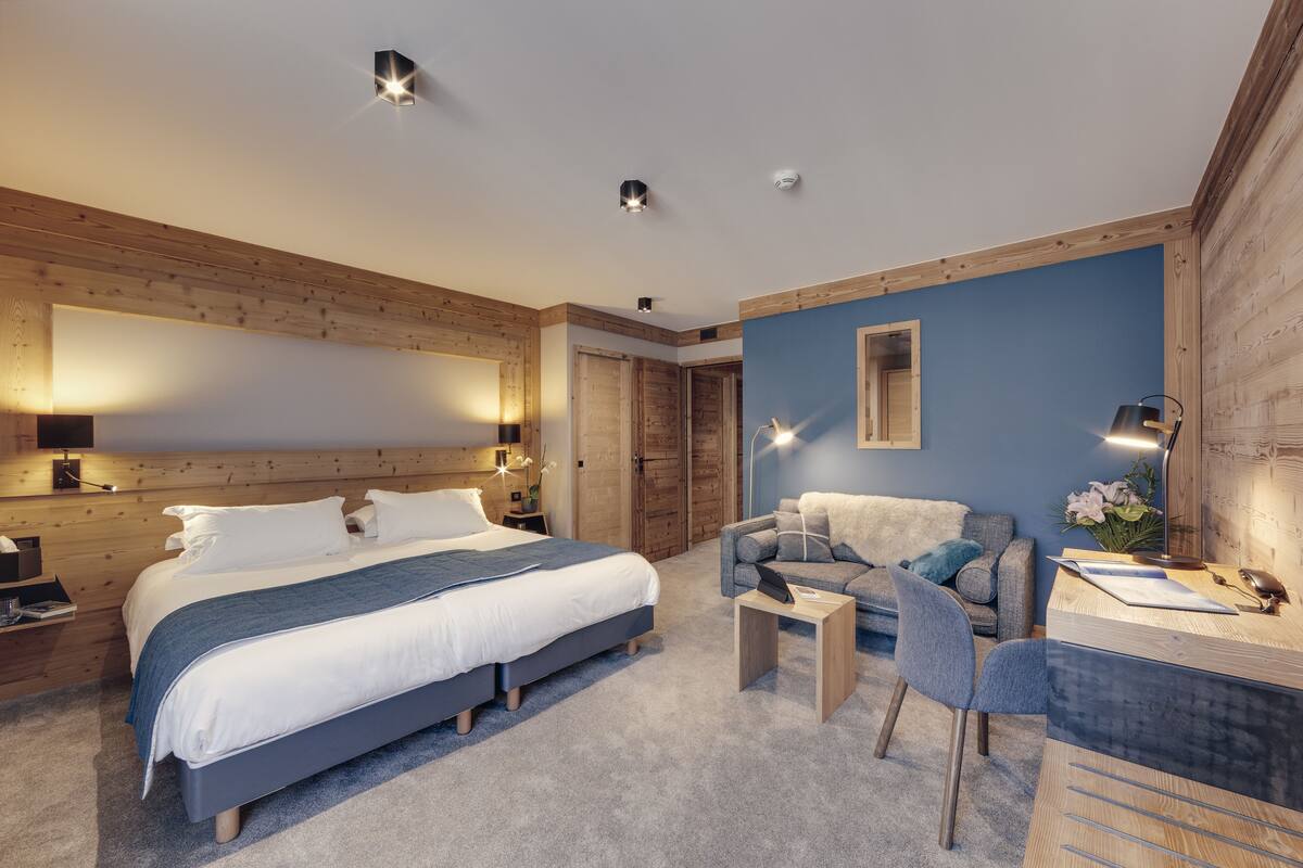 A modern bedroom with a large bed, a desk, and a chair. There are wooden walls and a blue accent wall.