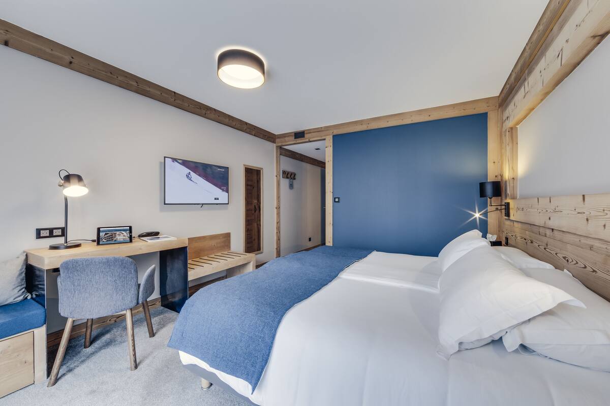A bedroom with a bed, desk, chair, and a blue accent wall.