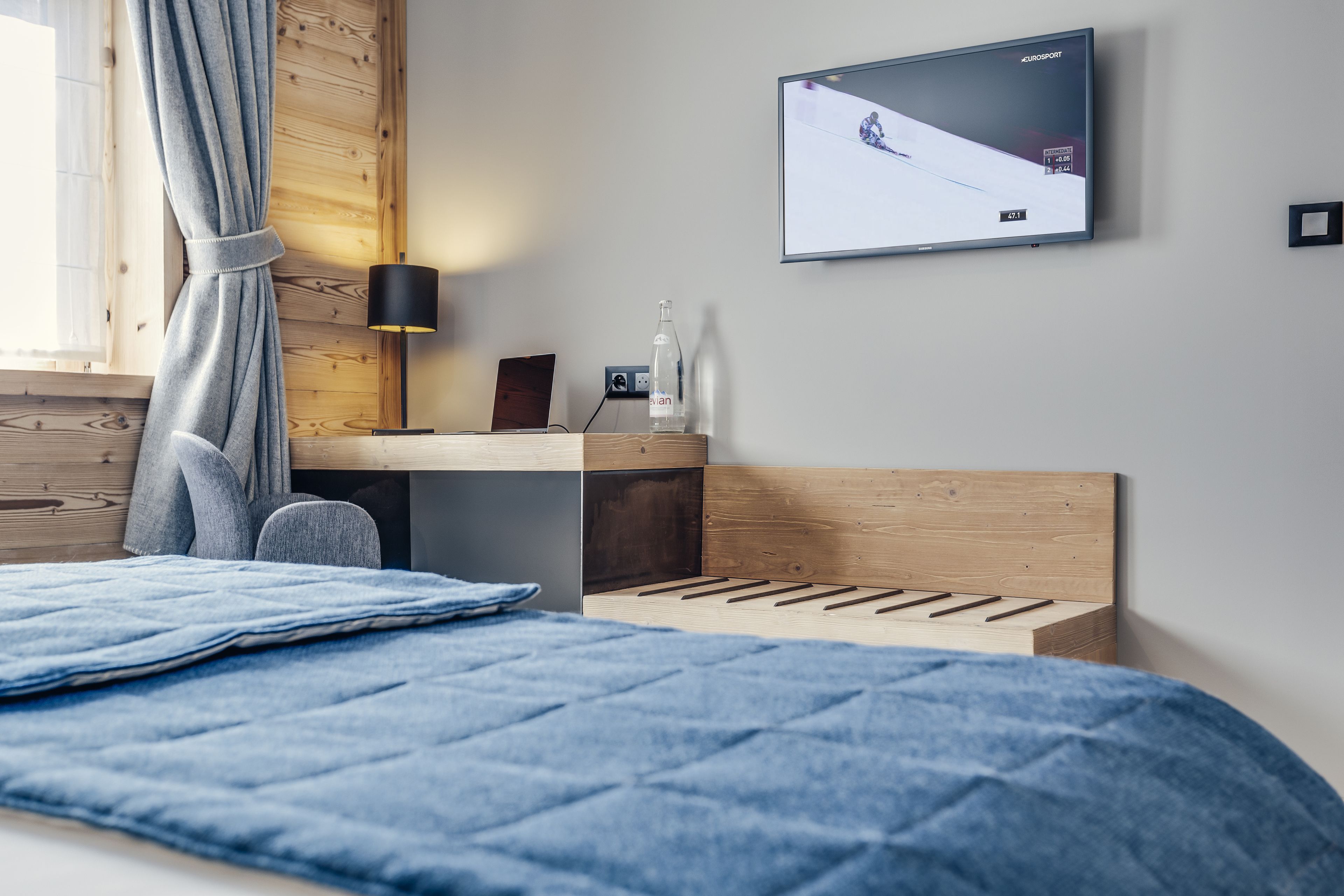 Un dormitorio moderno con cama, escritorio, televisor y ventana con cortinas.