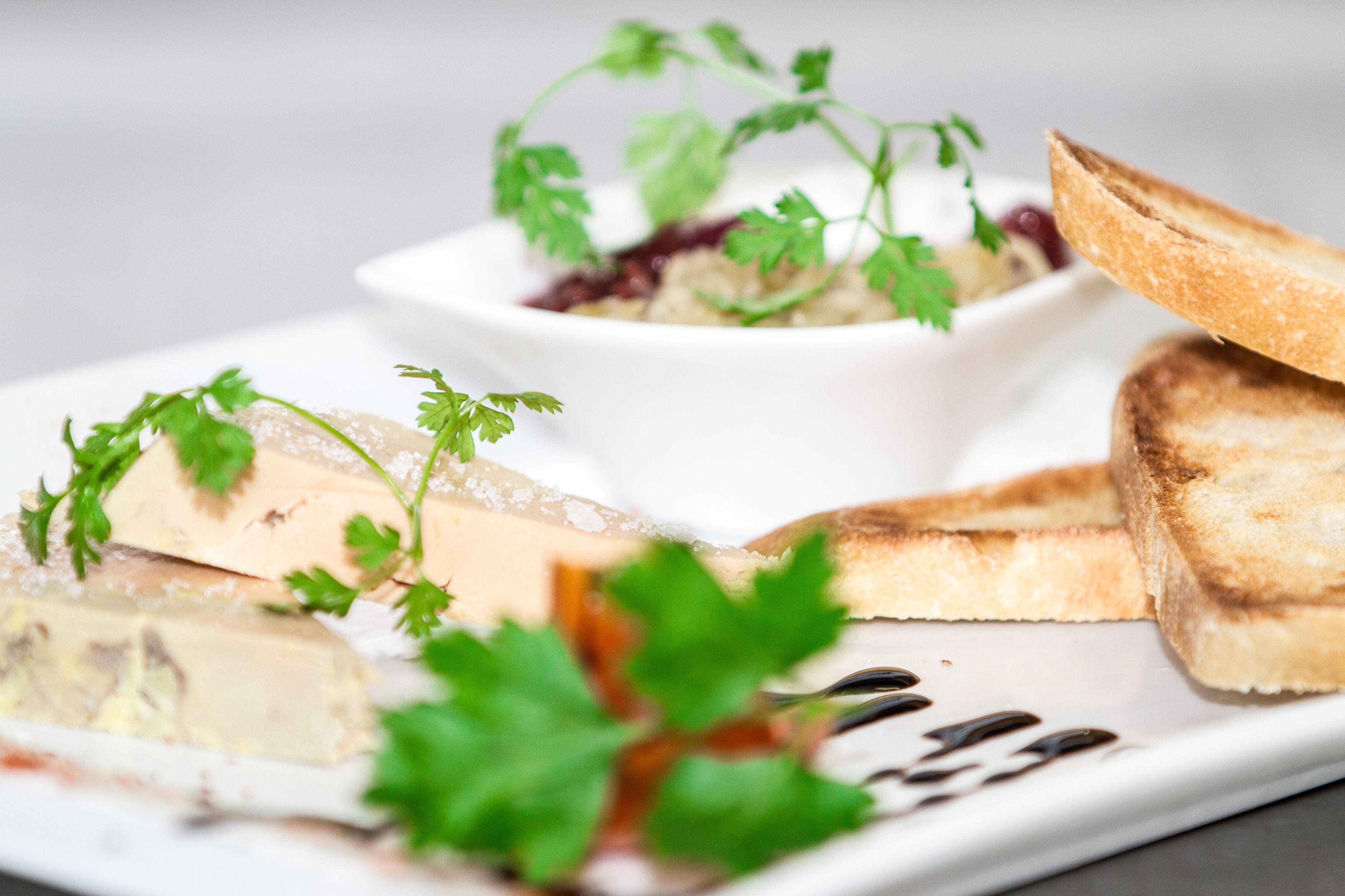 Une assiette contenant divers aliments, notamment un morceau de viande, une tranche de pain et un petit bol de sauce, le tout garni de persil.