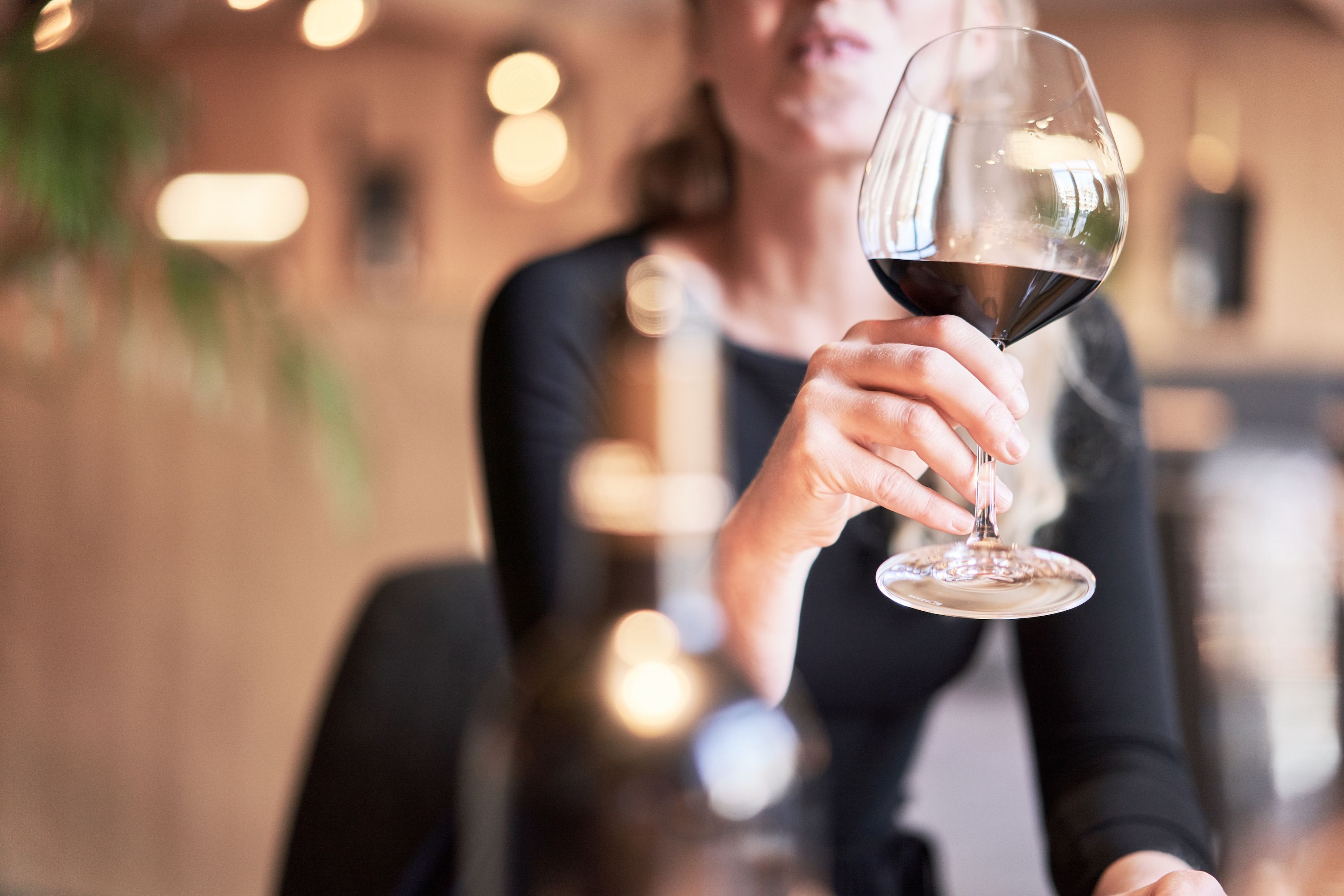 A person holding a wine glass in a dimly lit room with blurred background lights.