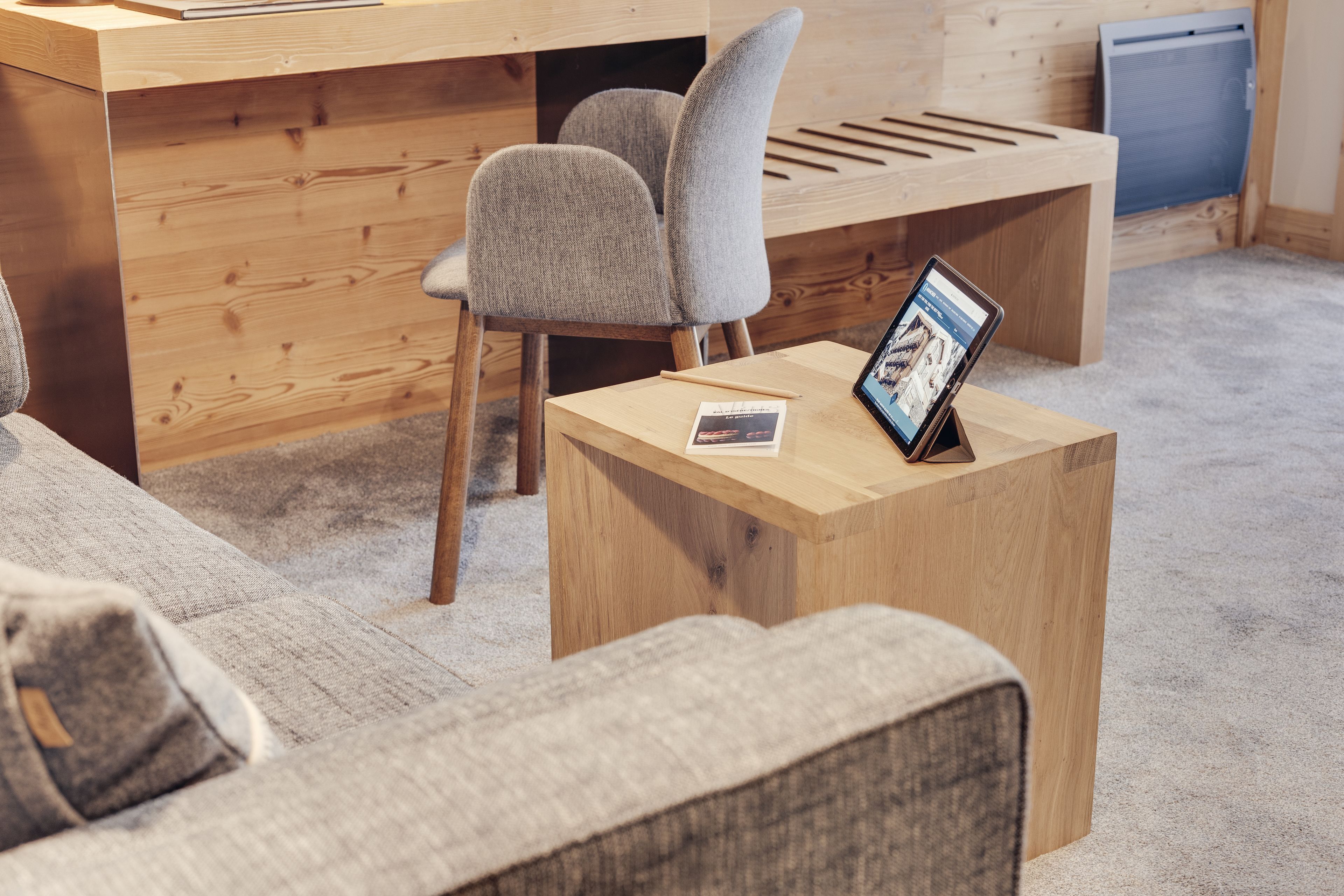 Une pièce moderne et minimaliste, dotée d’un bureau en bois, d’une chaise rembourrée de couleur grise et d’une petite table d’appoint.