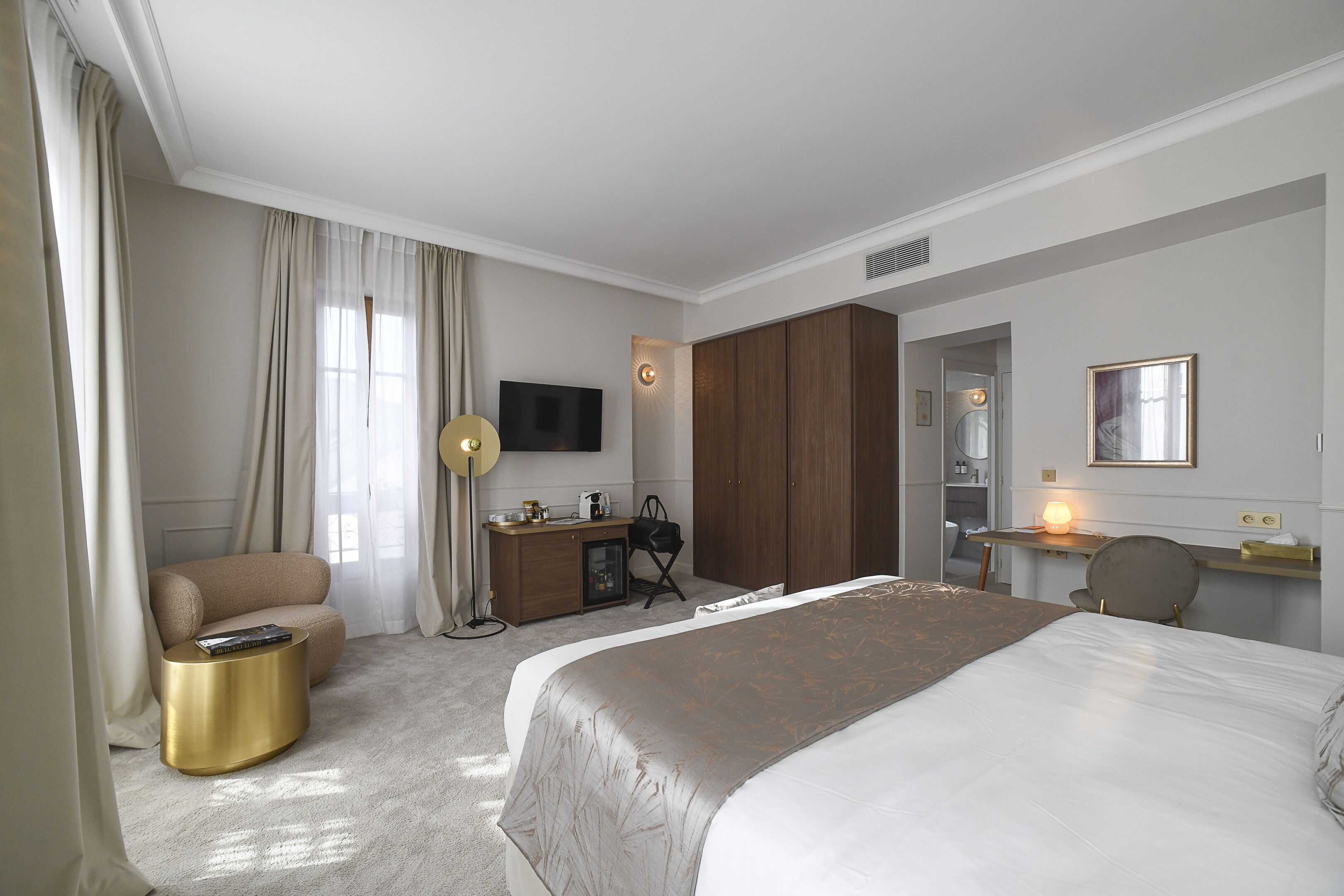 Ein Hotelzimmer mit einem großen Bett, einem Schreibtisch mit Stuhl, einem Kleiderschrank, einem Fernseher und einer Lampe.