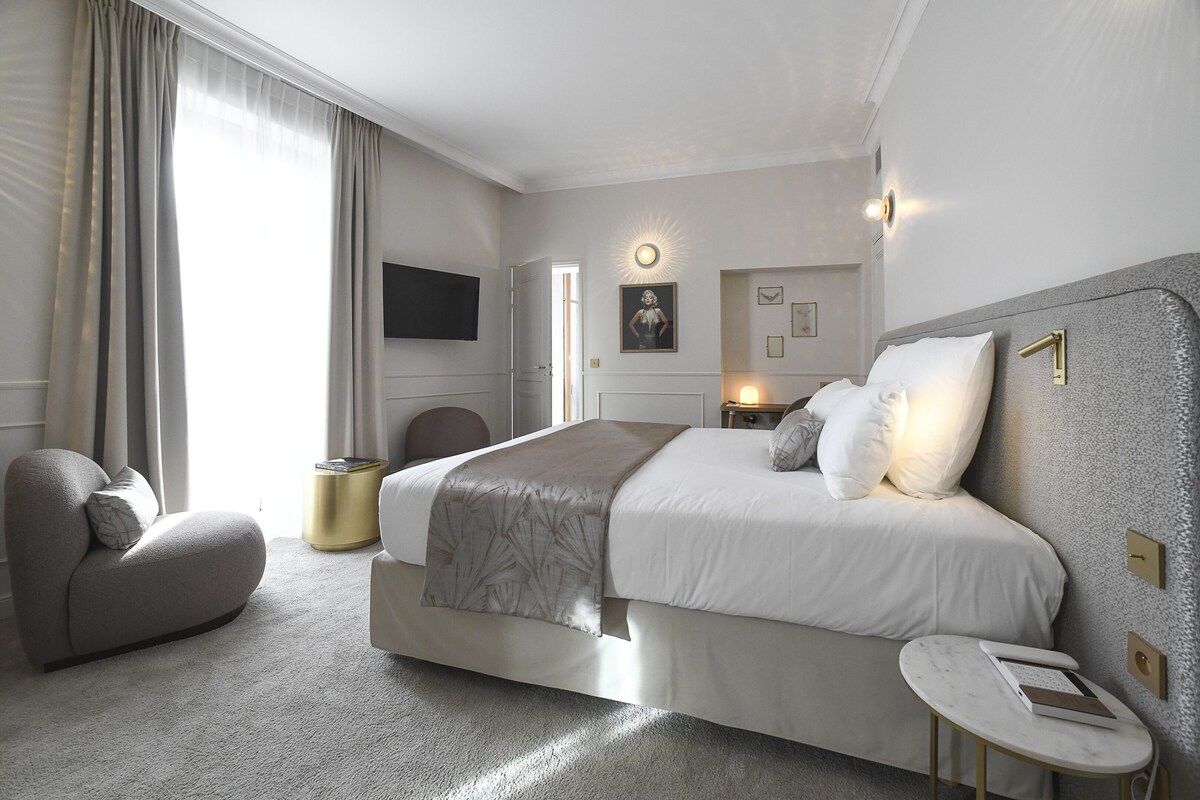 Een moderne hotelkamer met een groot bed, een zithoek, een flatscreen televisie en een nachtkastje met lamp.