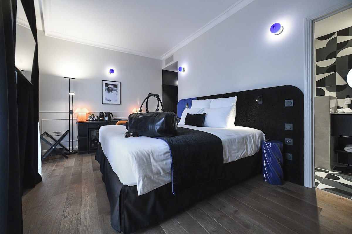 Een hotelkamer met een groot bed, een bureau met een lamp en een koffer op het bed.
