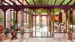 Une terrasse extérieure couverte, aménagée avec des tables et des chaises, entourée de plantes en pot et agrémentée d’une structure de pergola en bois.