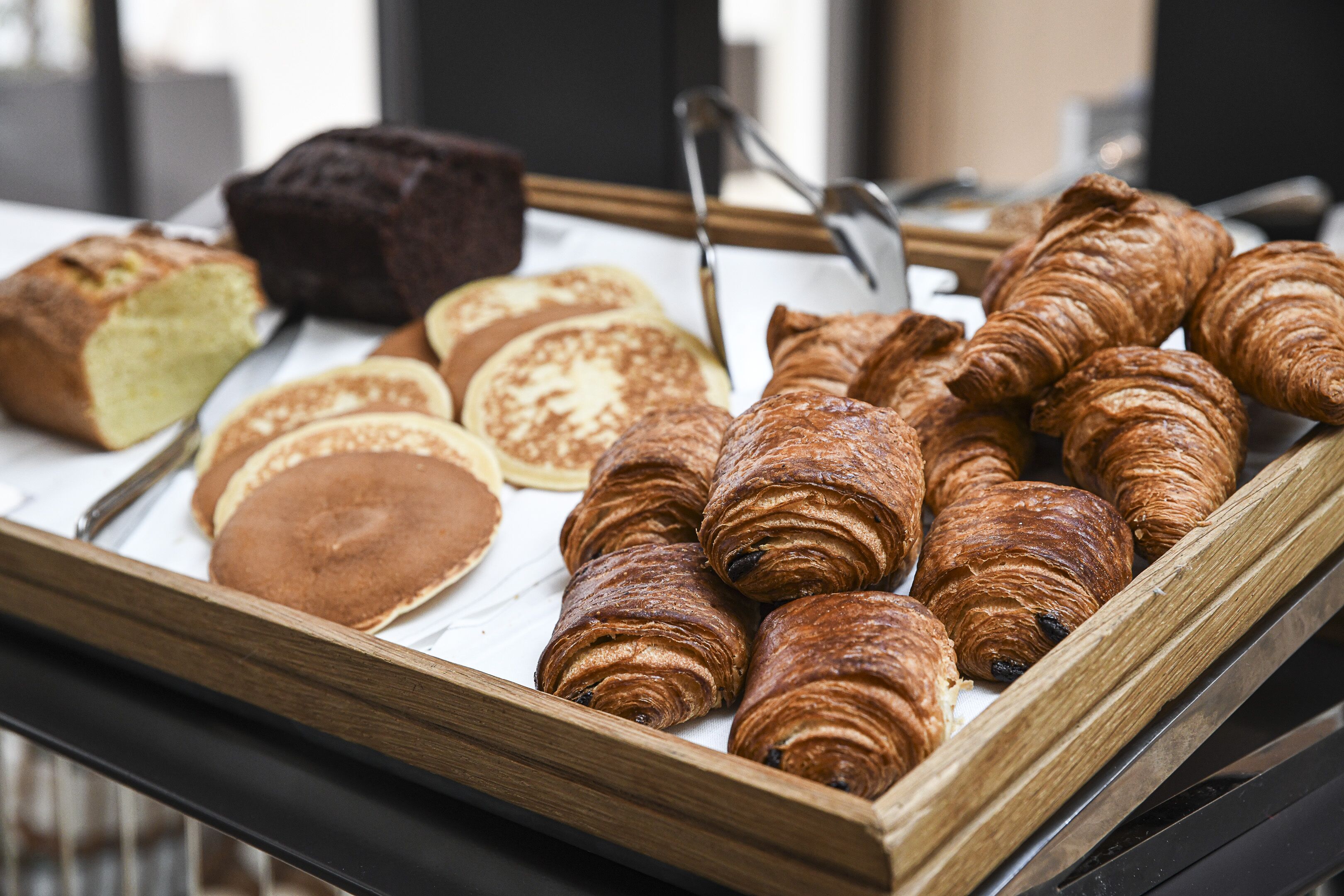 Un plateau contenant un assortiment de produits de boulangerie, notamment des croissants, une miche de pain et des crêpes.