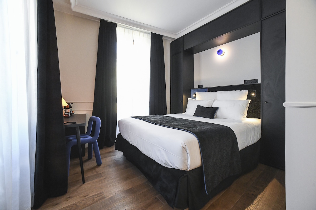 Een hotelkamer met een groot bed, een bureau met stoel en een raam met gordijnen.