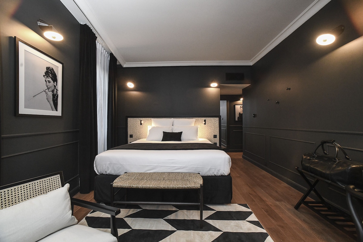 Een moderne hotelkamer met een groot bed, een bankje, een stoel en een ingelijste foto aan de muur.