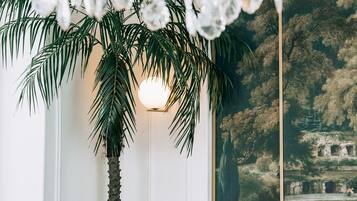 A room with a large painting of a landscape, a palm tree, and a table with bottles and a candle.