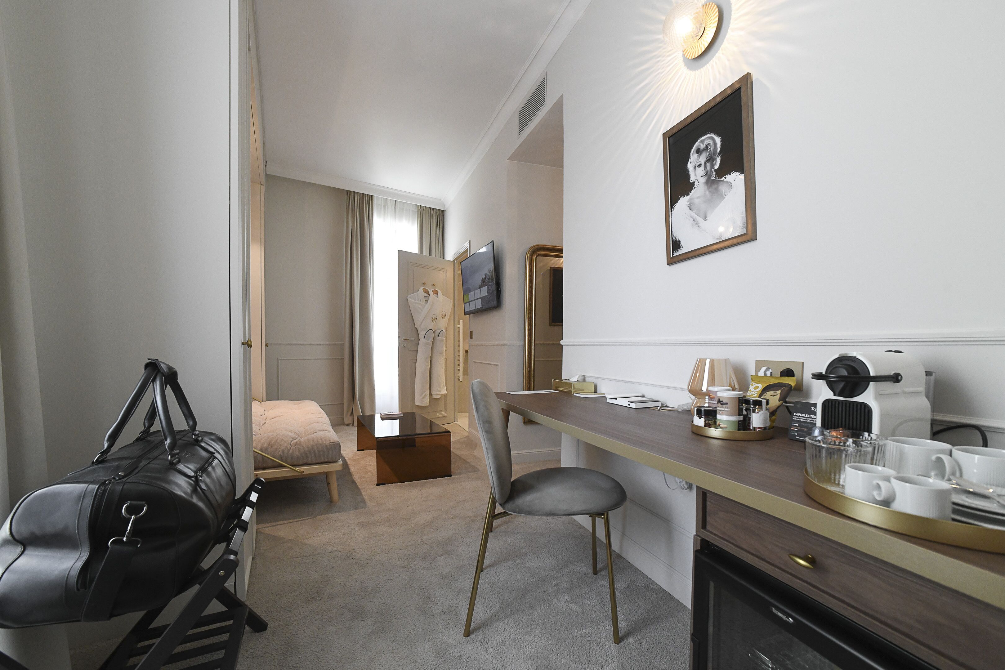 Une chambre d’hôtel avec un bureau, une chaise et un lit. Il y a un téléviseur accroché au mur et une fenêtre avec des rideaux.