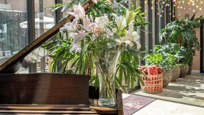 A grand piano in a spacious, sunlit room with large windows and hanging floral decorations. - Grand Hôtel du Parc (Aix-les-Bains)