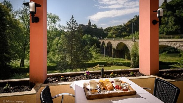 A table with breakfast items, a view of a bridge, and greenery. - Logis Hotel Restaurant Du Pont (Saint-Cirgue)