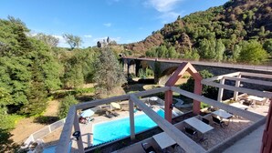 A pool area with lounge chairs and a stone deck, overlooking a forested valley and a stone bridge. - Logis Hotel Restaurant Du Pont (Saint-Cirgue)