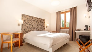 A hotel room with a bed, a wooden chair, a desk, a radiator, and a window with curtains. - Logis Hotel Restaurant Du Pont (Saint-Cirgue)