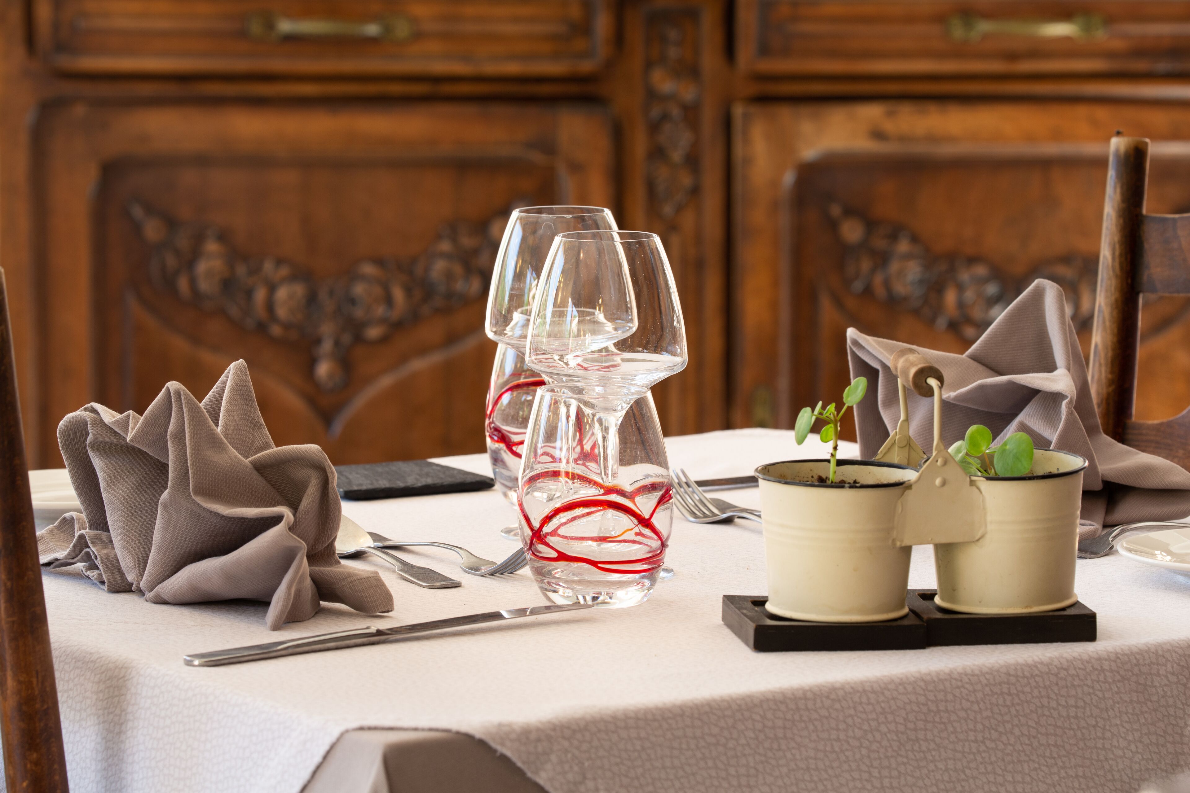 A table set with wine glasses, a vase with red string, and two small potted plants.
