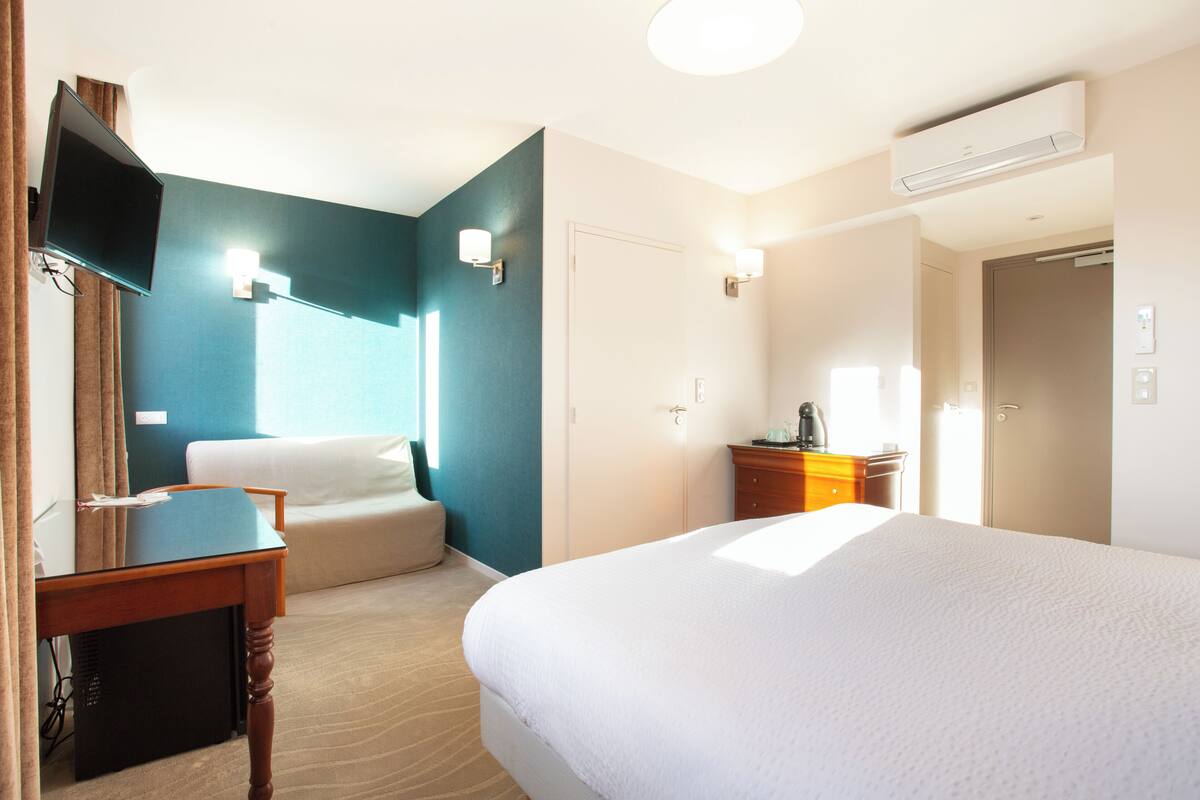 Una habitación de hotel con cama, escritorio, silla, televisor y cómoda.
