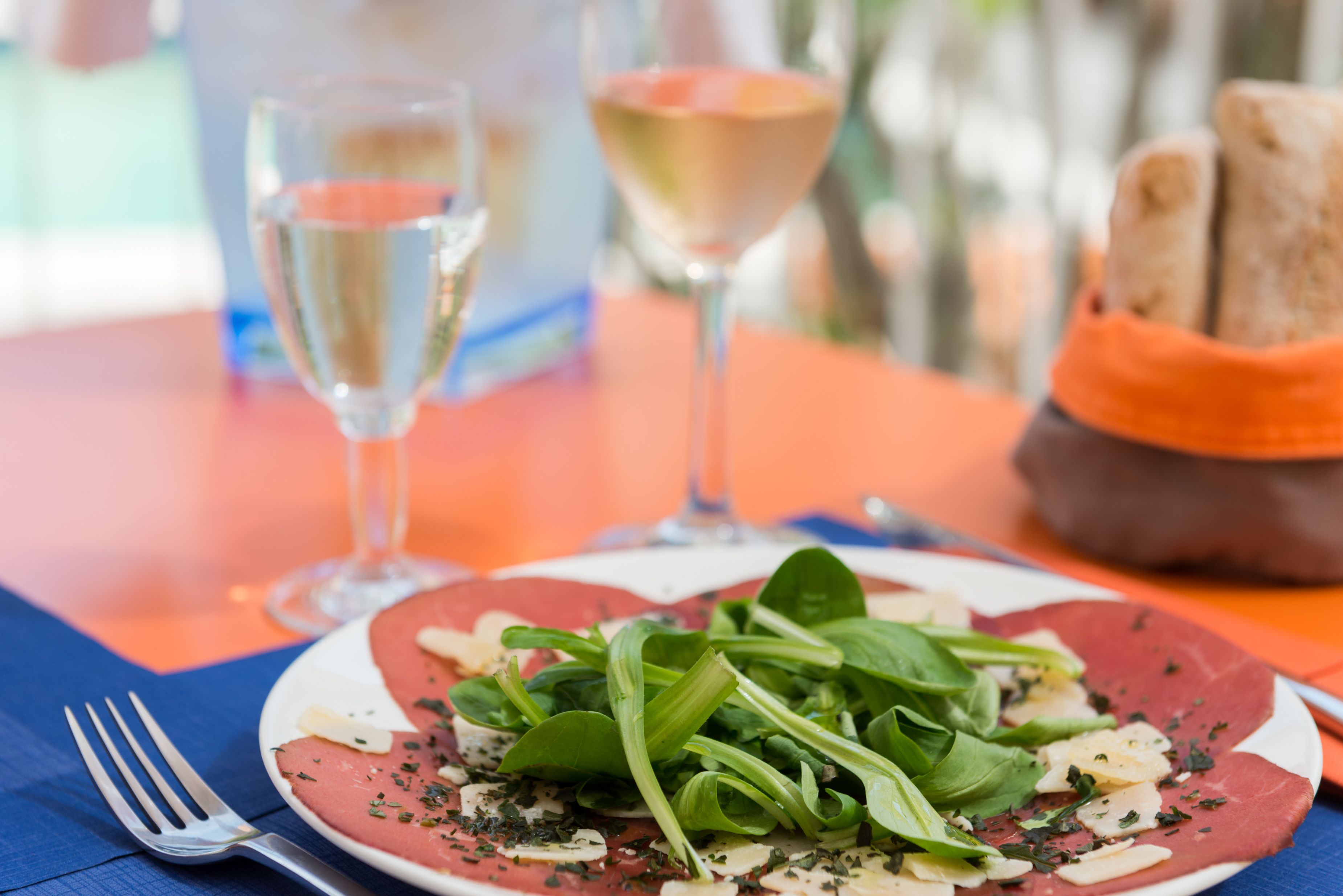 A plate of food with a fork and two glasses of white wine on a table.