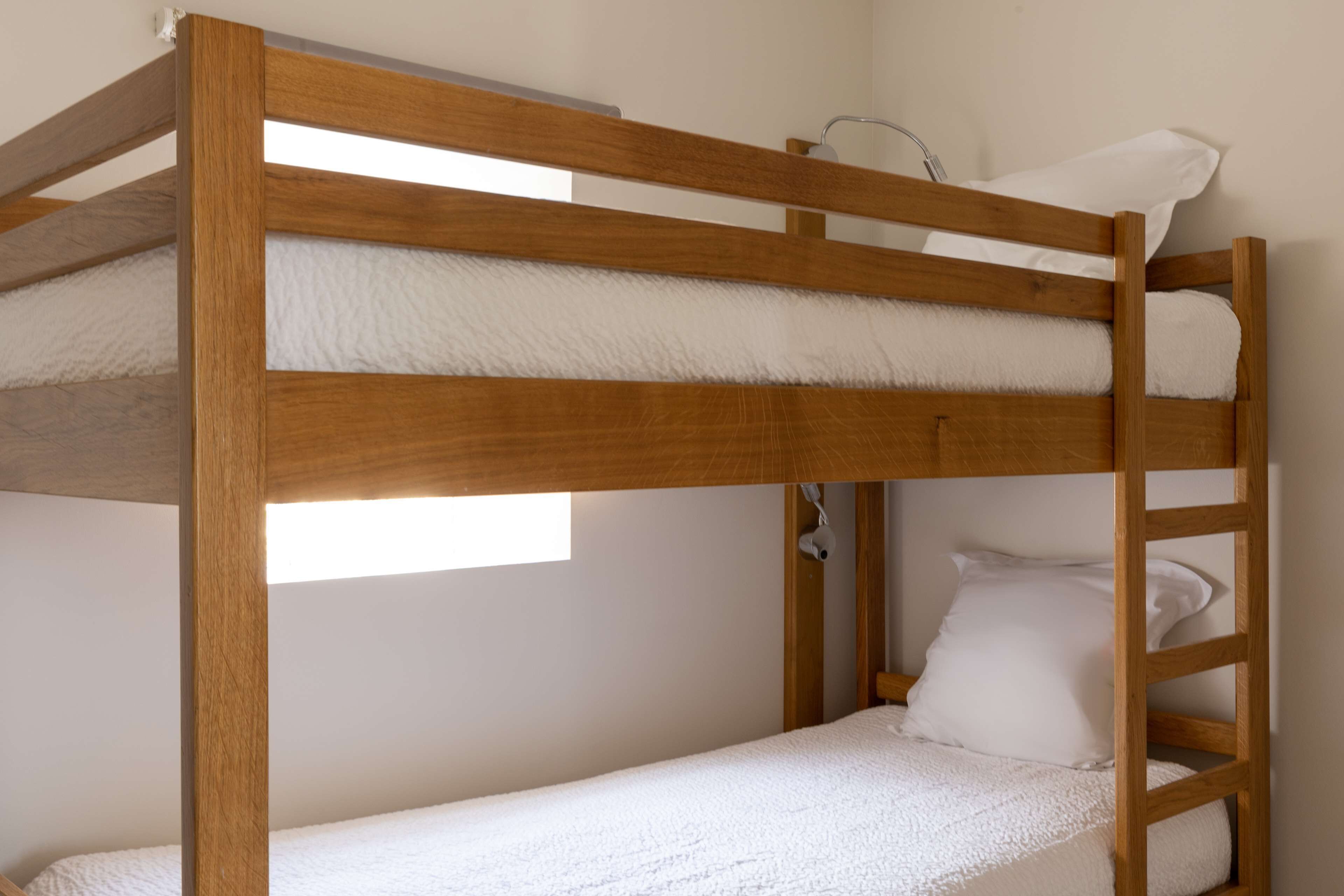Una cama litera con ropa de cama blanca y una ventana encima.