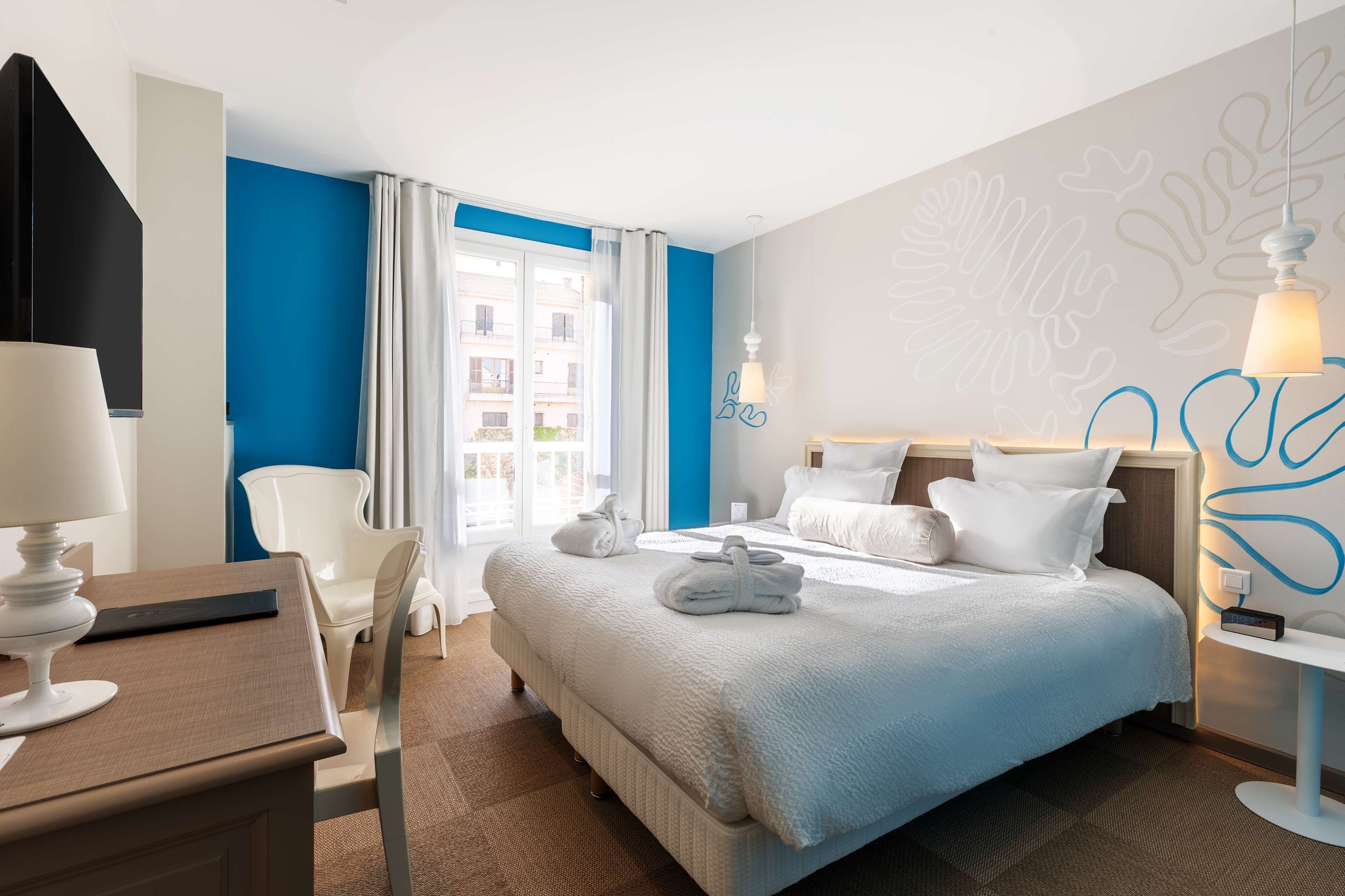 Een hotelkamer met een bed, een bureau, een stoel, een lamp en een raam met gordijnen.