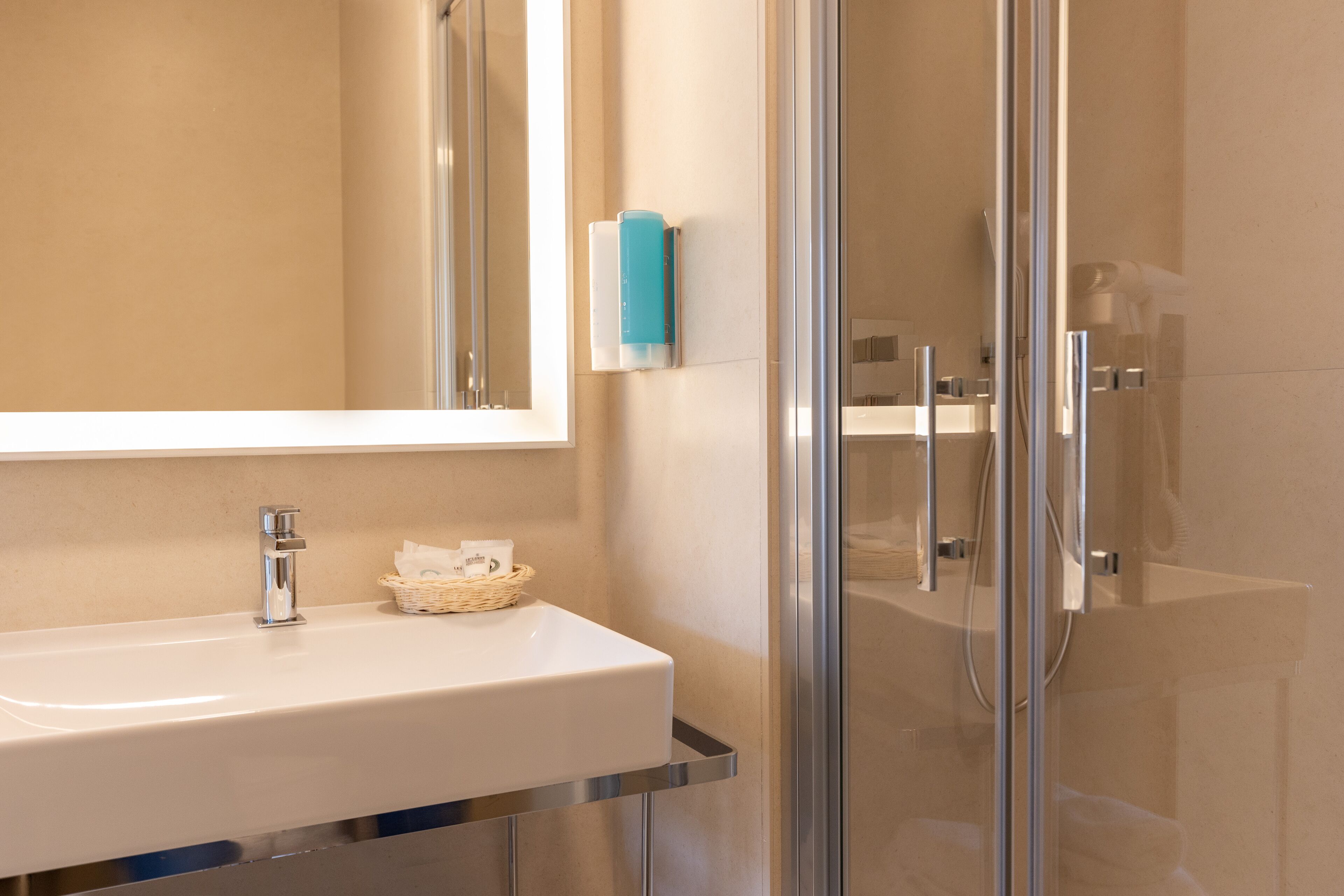 A modern bathroom with a white sink, chrome fixtures, a glass shower enclosure, and a blue soap dispenser.