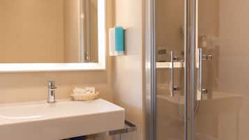 Un baño moderno con un lavamanos blanco, accesorios cromados, cabina de ducha con mampara de vidrio y un dispensador de jabón azul.