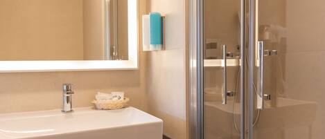 A modern bathroom with a white sink, chrome fixtures, a glass shower enclosure, and a blue soap dispenser.