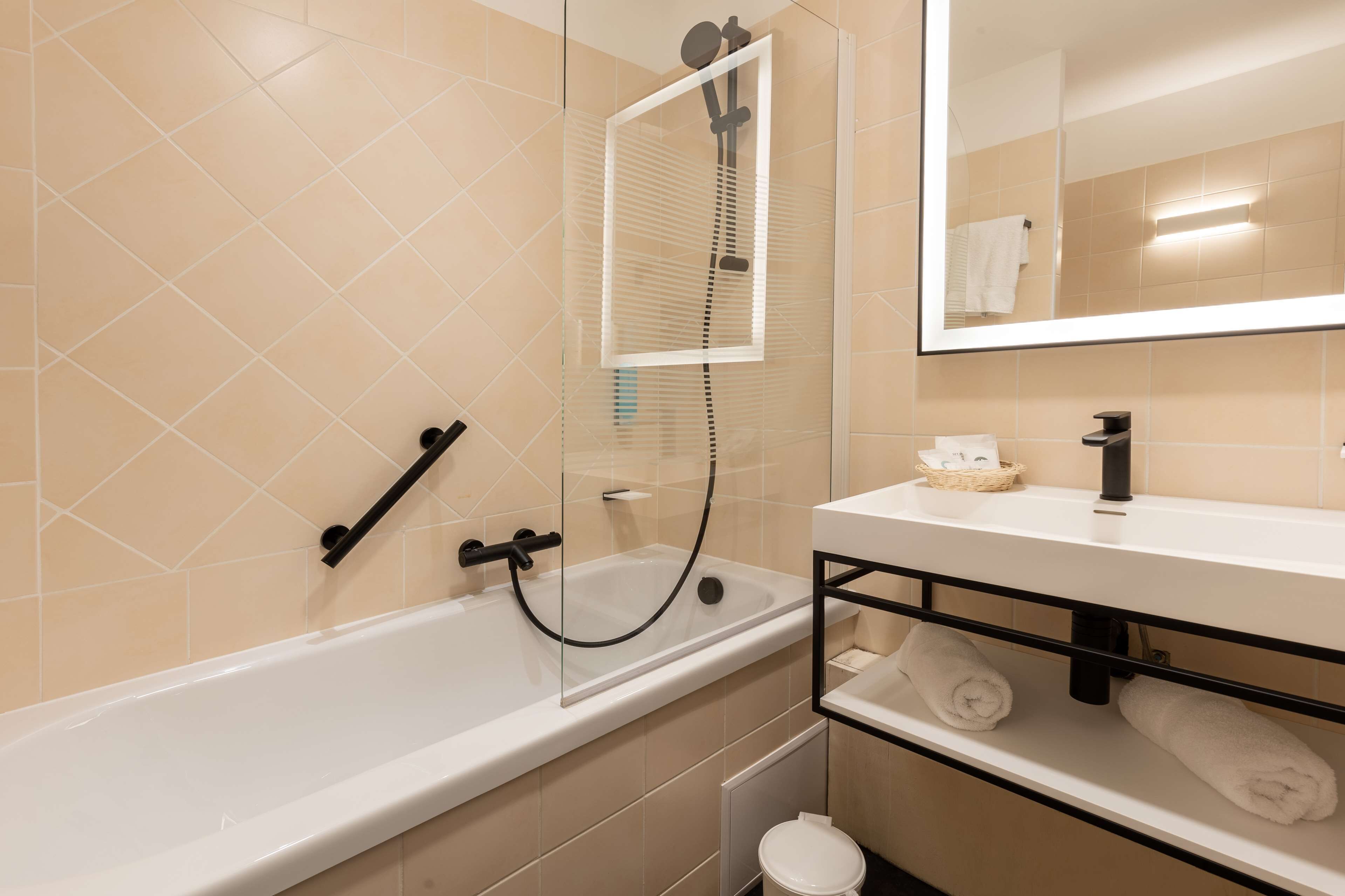 A modern bathroom with a bathtub, a glass-enclosed shower, and a white sink with a black faucet.