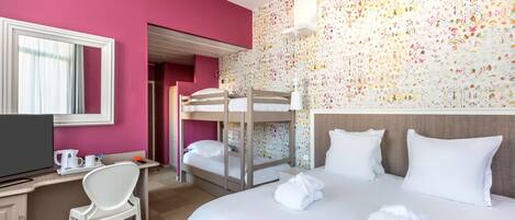 A hotel room with a bunk bed, a desk with a chair, a television, and a large bed with pillows and towels.