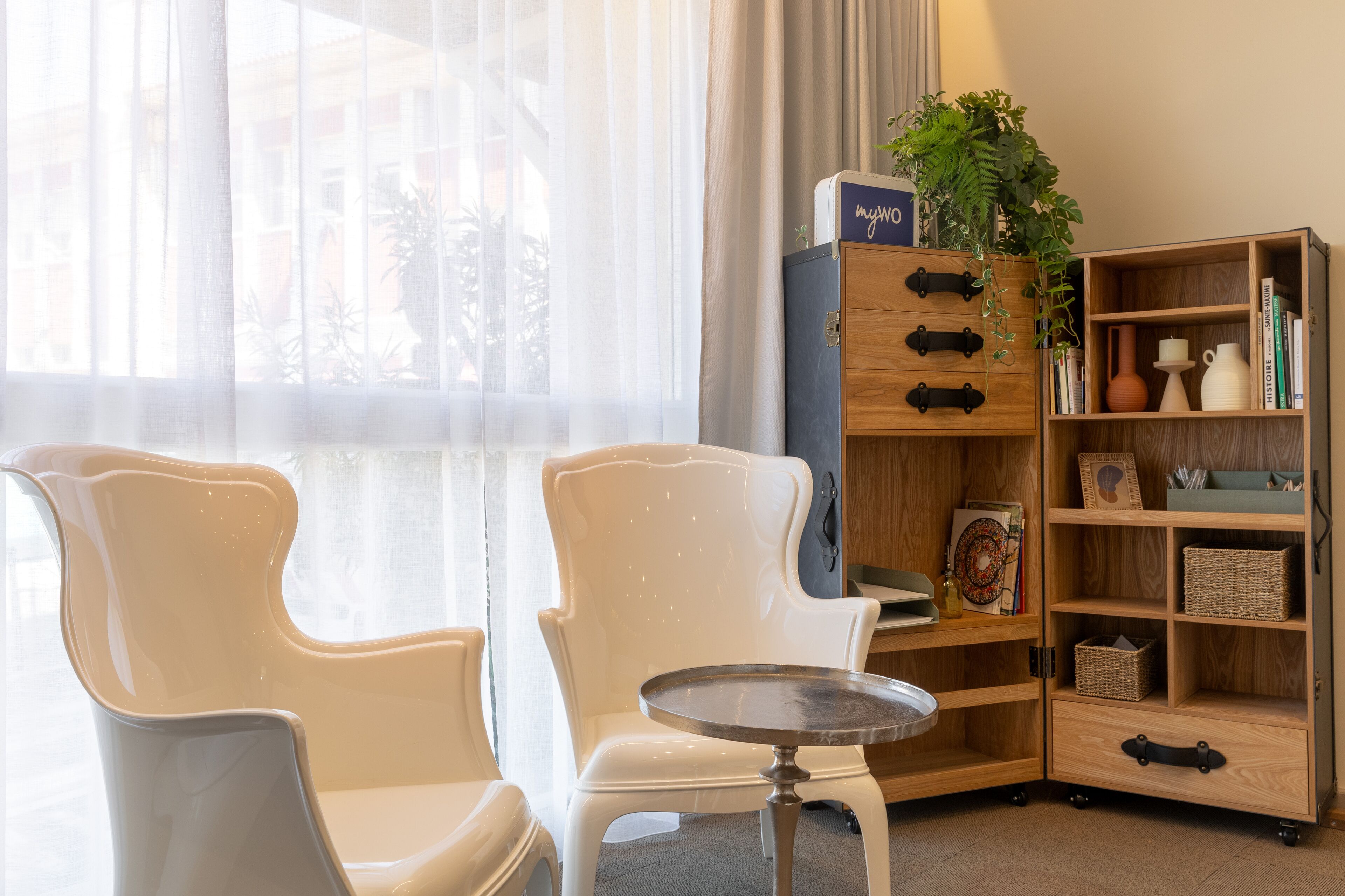 Une pièce comprenant deux chaises blanches, une petite table ronde et un meuble en bois doté d’étagères.
