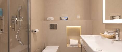 A modern bathroom with a glass-enclosed shower, a white toilet, a sink with a basket of toiletries, and a mirror above the sink.