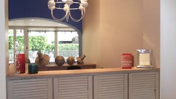 A hotel reception area with a modern chandelier, a counter with decorative items, and a view of greenery outside.
