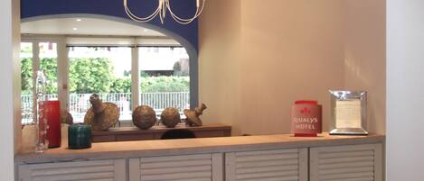 A hotel reception area with a modern chandelier, a counter with decorative items, and a view of greenery outside.