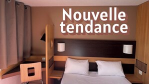 Een hotelkamer met een bed, een stoel, een bureau en een wandlamp.