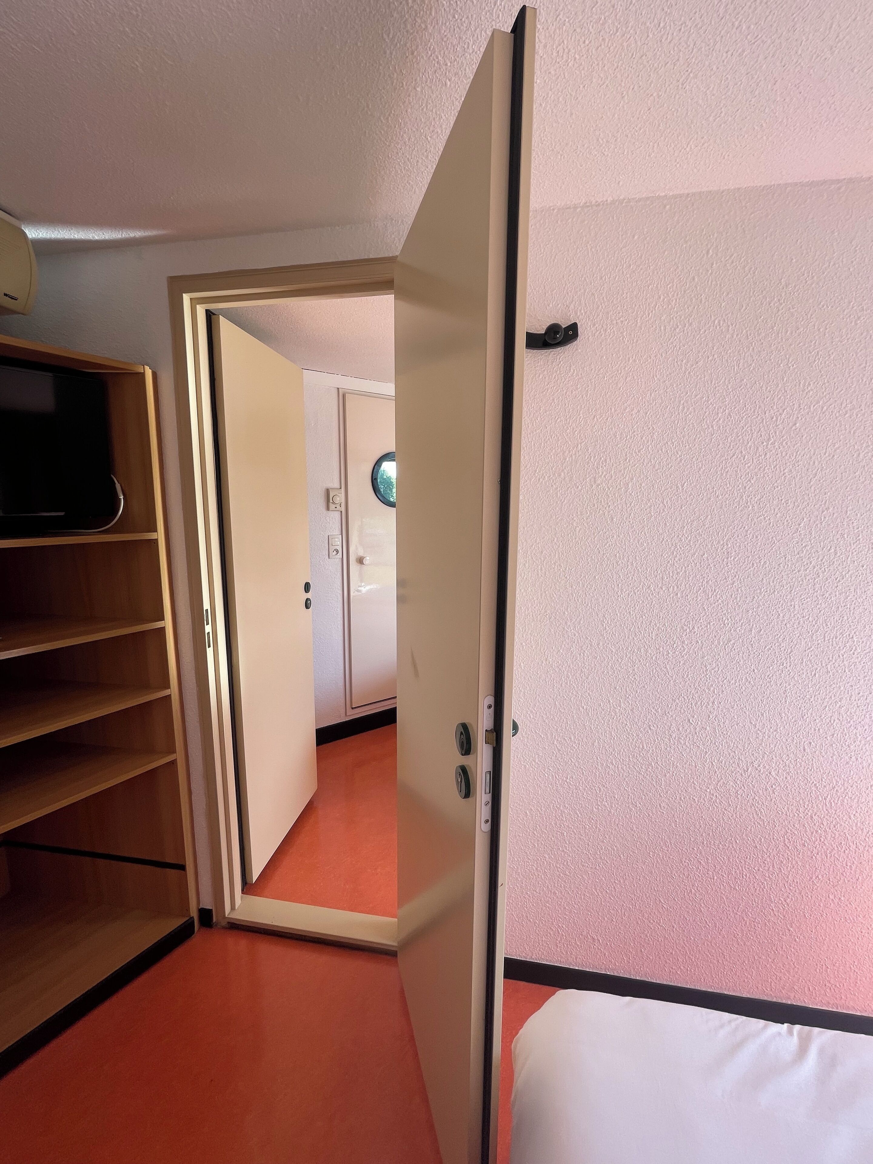 A room with a bed, a wardrobe, and a door leading to another room.