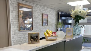 Een receptiebalie met een witte bakstenen muur, ingelijste foto's, een vaas met bloemen en een presentatie van ingeblikte producten.
