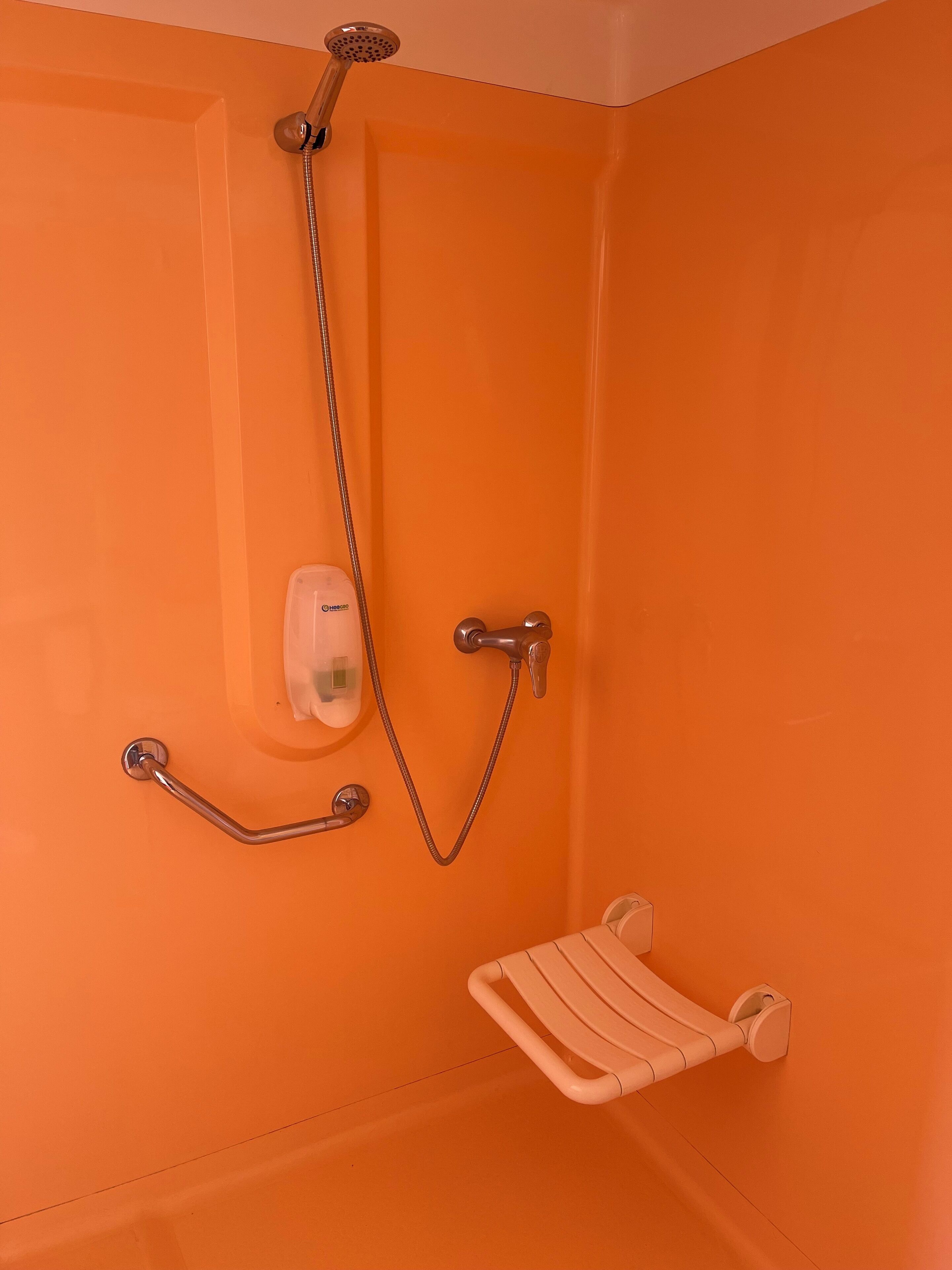Un bagno con una parete arancione, una doccia con soffione a mano e un maniglione bianco.