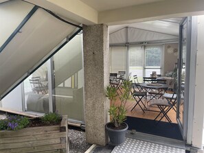 Un espacio al aire libre cubierto con mesas y sillas, una planta en maceta y un banco de madera.