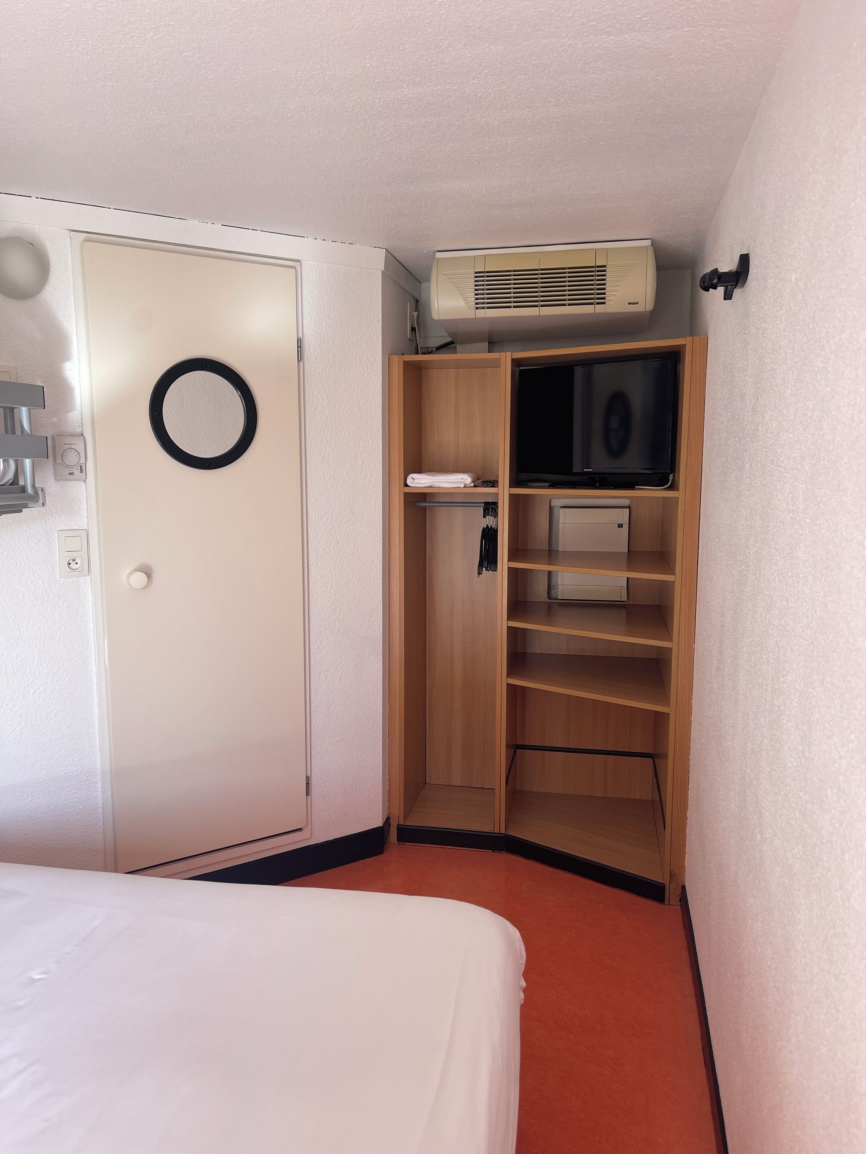 Una habitación de hotel con cama, armario y aire acondicionado integrado.
