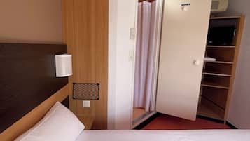 Hotellihuone, jossa on sänky, puinen vaatekaappi, televisio ja kattotuuletin.