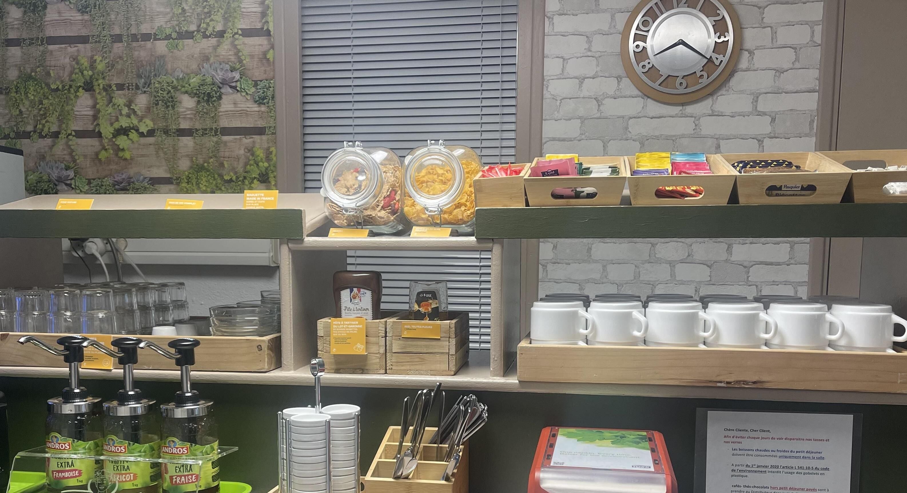 Mostrador de cafetería con botes de granola, un reloj y varios tipos de tazas de café.