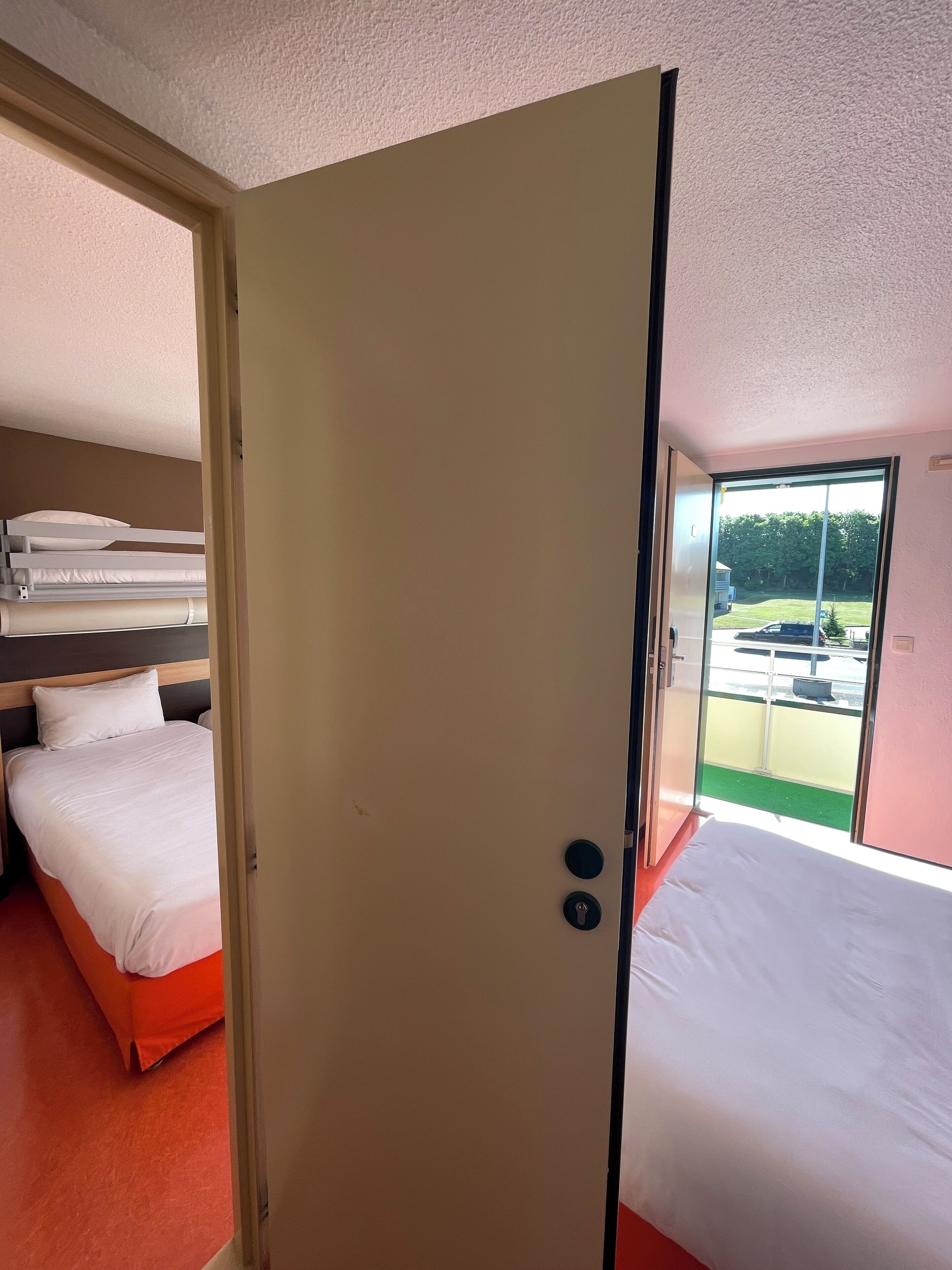 Habitación de hotel con una cama, una litera y una puerta corrediza de vidrio que da a un balcón.
