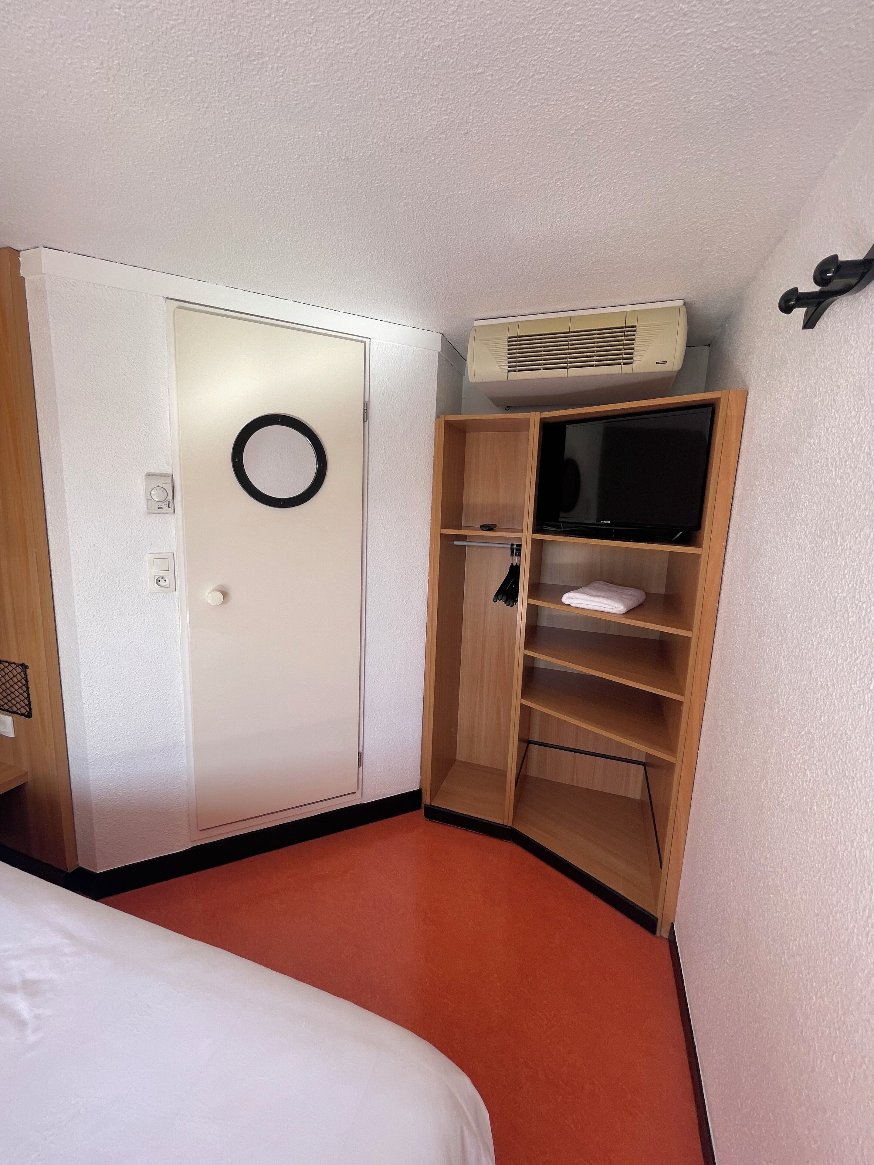 A hotel room with a bed, a wardrobe, a mirror, and an air conditioning unit.