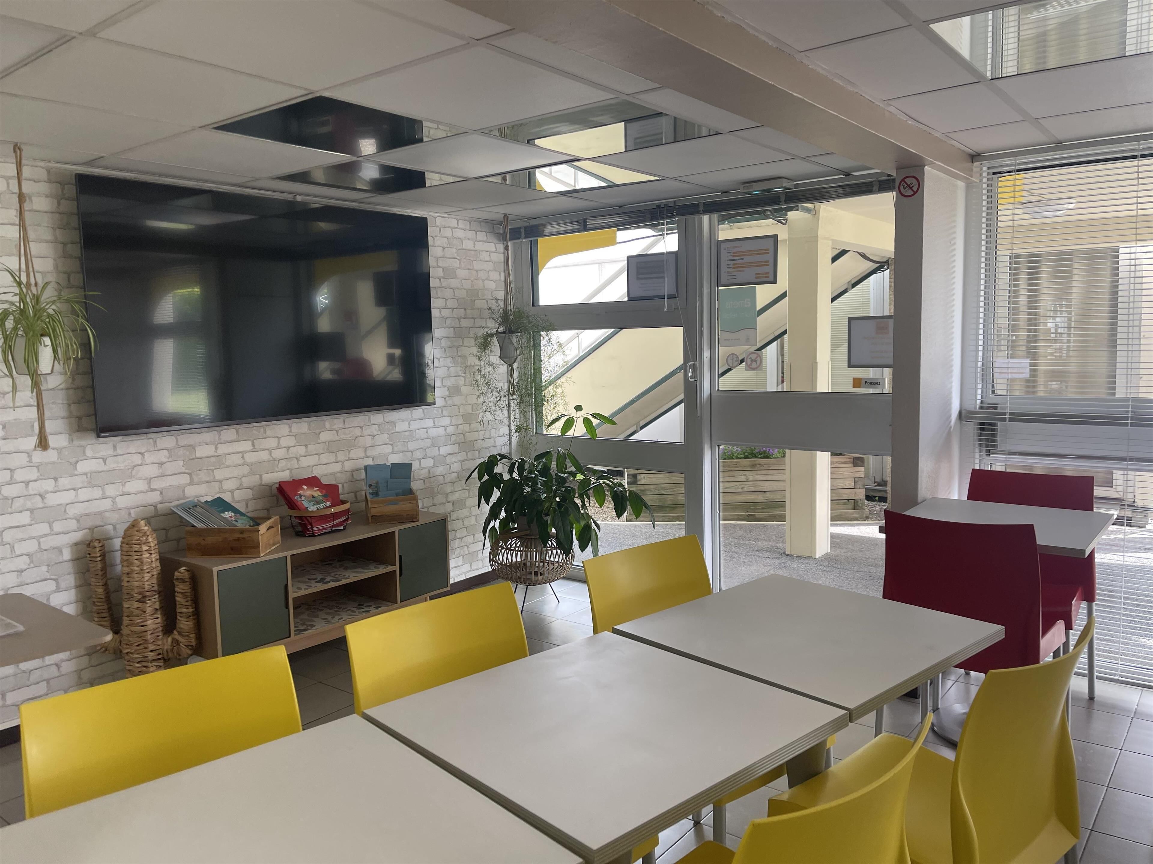 Ein modernes Interieur mit weißen Backsteinwänden, einem Flachbildfernseher, gelben Stühlen und einer Treppe, die in einen Außenbereich führt.